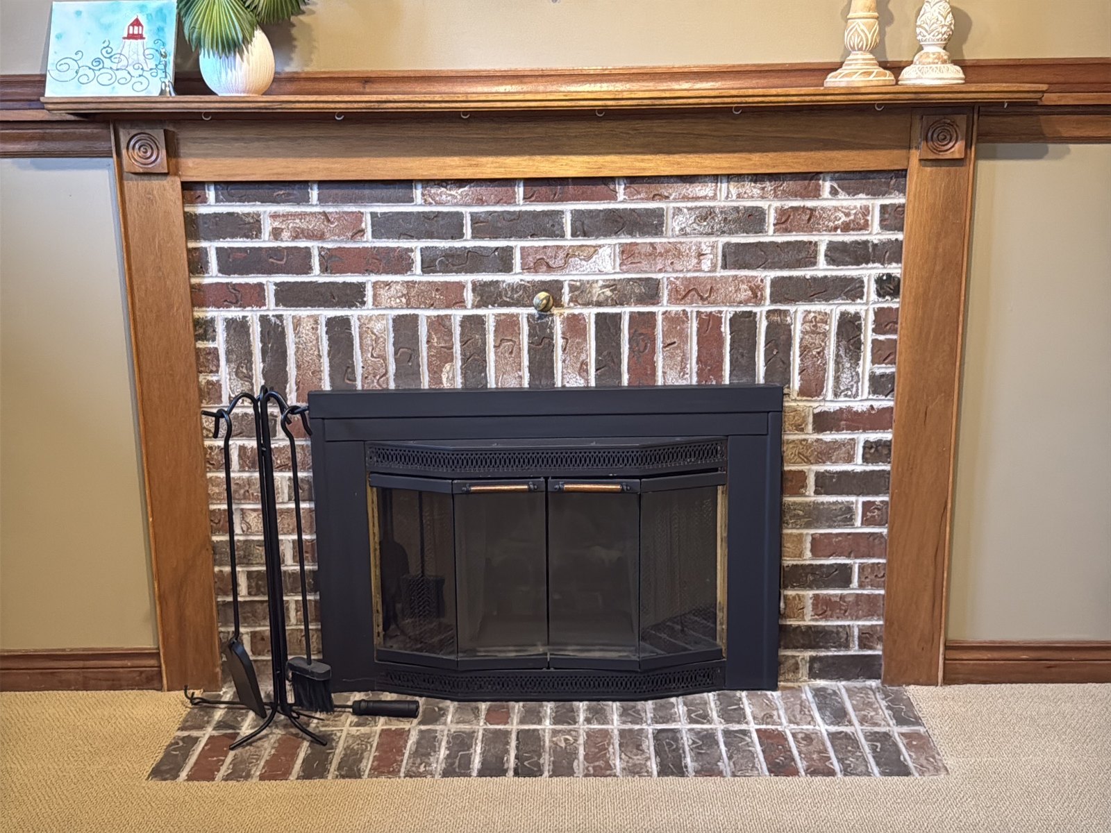 A masonry fireplace with a wood mantel, glass doors across the opening and a brick hearth in front of it