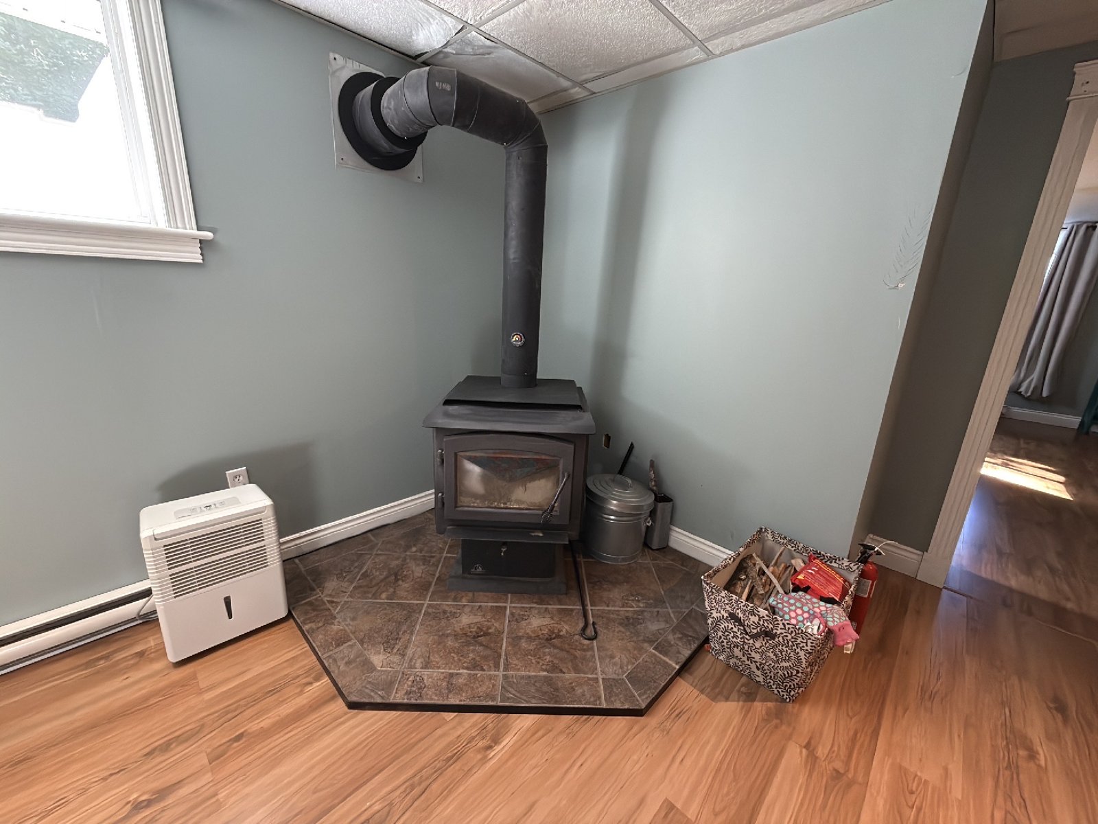 A wood stove in the corner of a finished room, standing on a tiled hearth pad, with its flue pipe running up and into the chimney through the wall