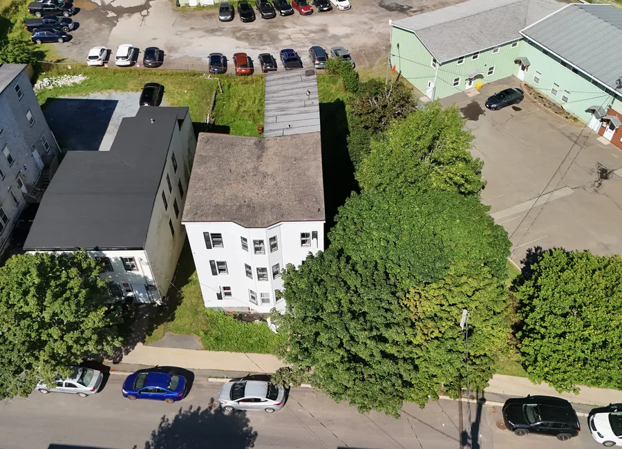 Aerial drone view of an older white three storey home with a low slope roof beside neighbouring buildings in Saint John, New Brunswick