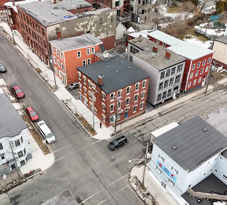 Aerial drone view of a residential intersection in Saint John New Brunswick showing brick and clapboard multi-unit buildings with flat and pitched rooftops during late winter