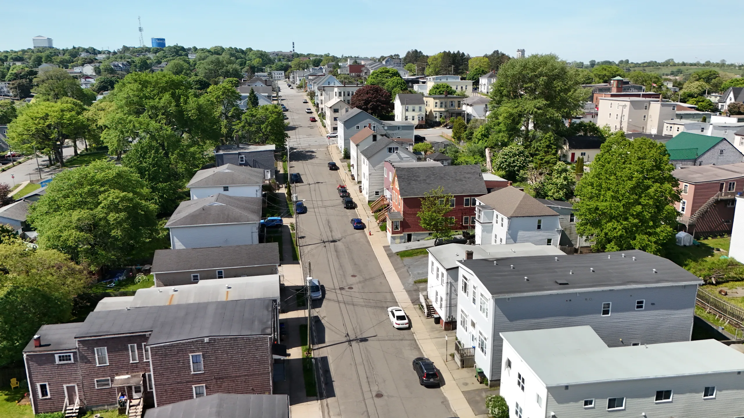 Aerial view of an older West Side Saint John residential street in early summer, the 1970s housing stock where clay and cast iron sewer lines are reaching the end of their service life